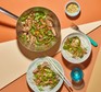 A pot and two plates of beef stir-fry on noodles, next to a glass and peanuts