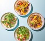 Four bowls with a grain mix of bulgur and quinoa with various toppings