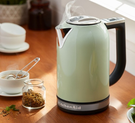 A steaming kettle on a wooden kitchen worktop next to a cup of loose-leaf tea