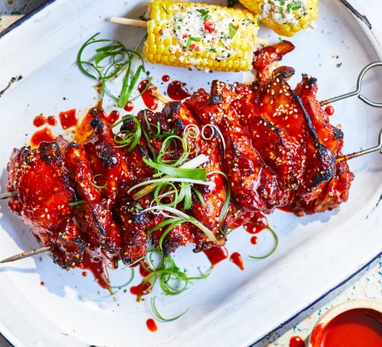 Korean chicken on skewers next to corn on the cob