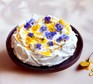 A lemon curd pavlova decorated with edible flowers on a cake stand