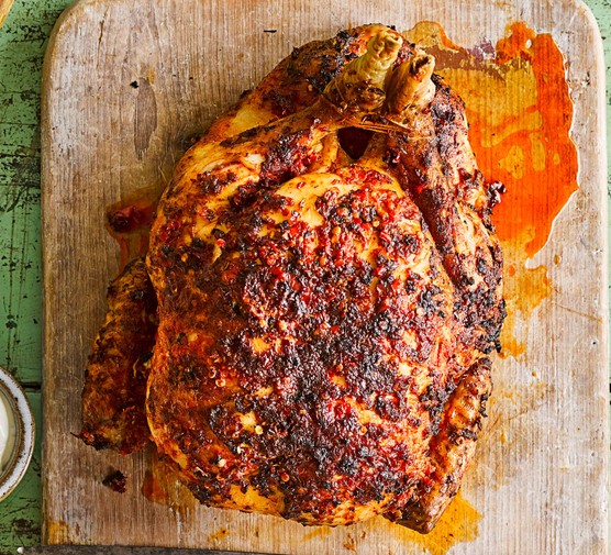 A whole chicken roasted in piri-piri spices, presented on a wooden chopping board