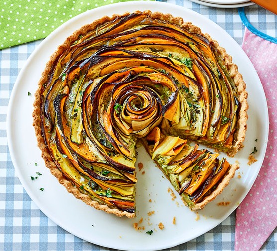 Tart with shaved vegetables in spiral pattern on a white plate