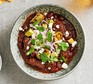 A bowl of chilli con carne garnished with chopped avocado, red onion and coriander